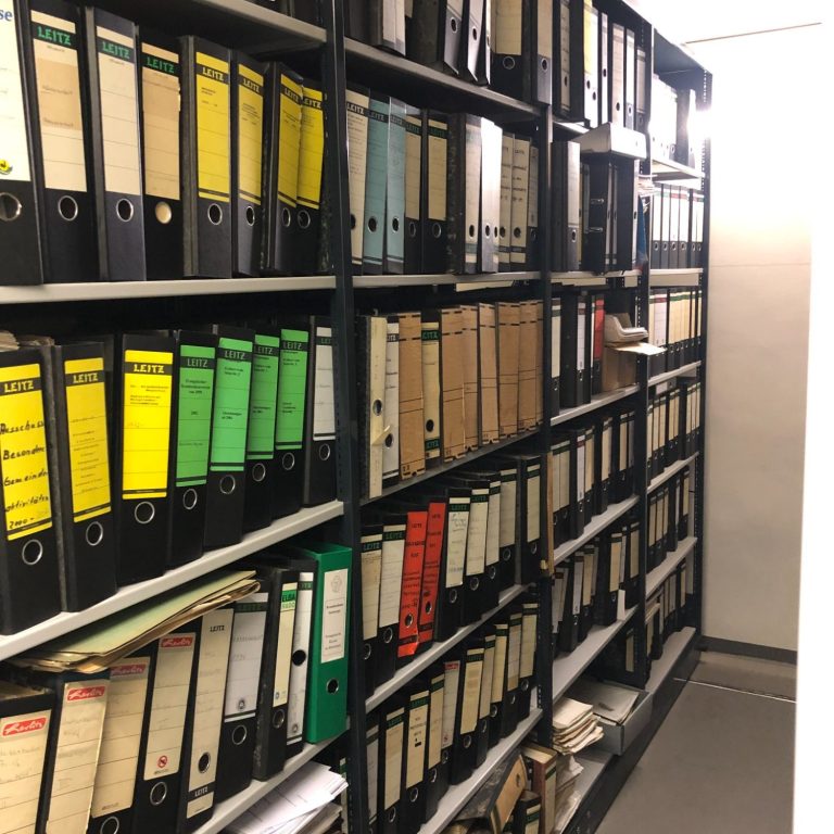 Regale mit Aktenordnern in verschiedenen Farben, ordnungsgemäß in Regalen sortiert.